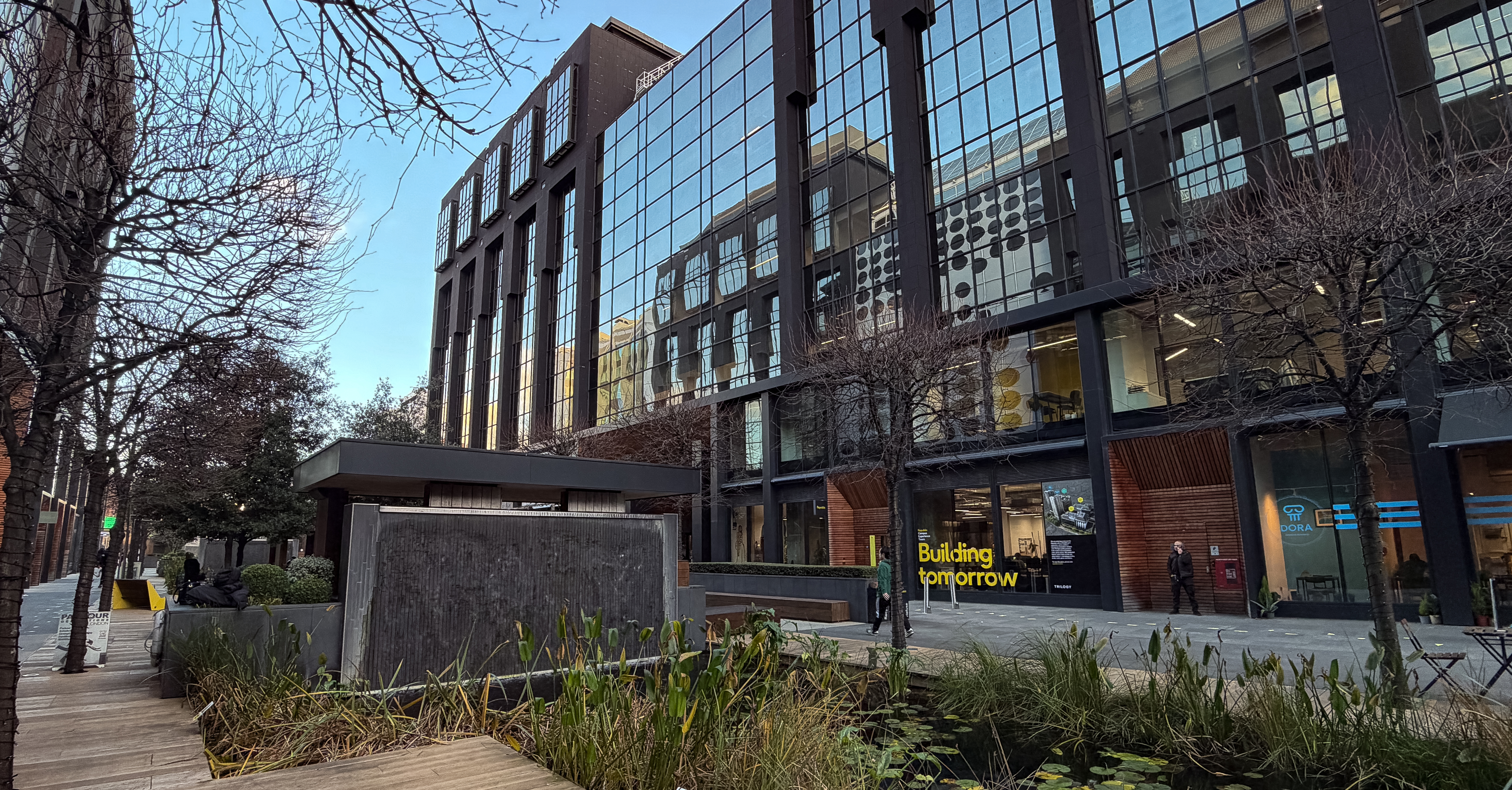Sunny evening looking at the modern buildings of the london campus with trees and a pond in the middle